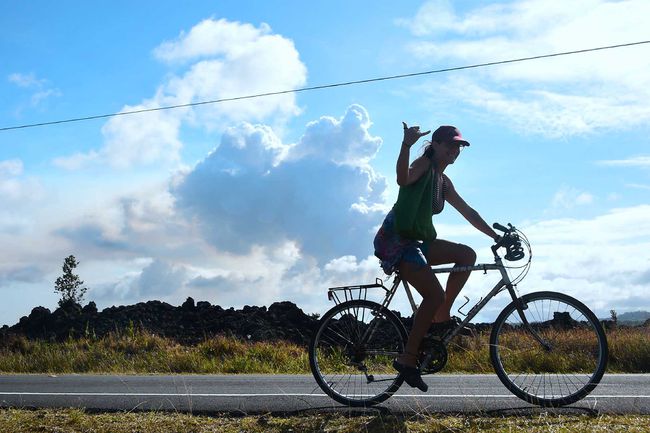Un cycliste offre le panneau Shaka, également connu sous le nom de "Hang Loose" en passant devant un panache de fumée volcanique au loin au-dessus de la zone de Leilani Estates près de la ville de Pahoa