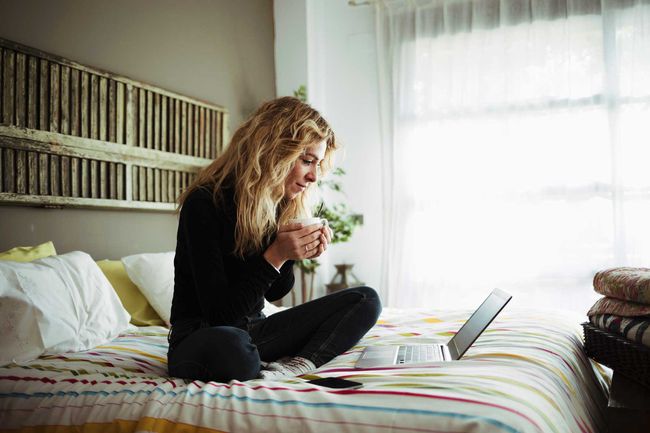 Femme utilisant un ordinateur portable assis sur le lit à la maison