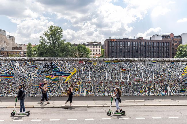 Les gens font du scooter près de la East Side Gallery, une galerie en plein air sur la plus longue section du mur de Berlin, le 03 juillet 2021 à Berlin, en Allemagne.