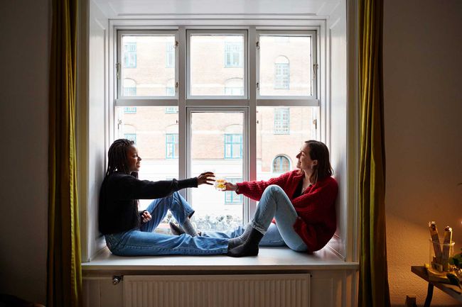 Jeunes colocataires portant un toast à des cocktails dans la fenêtre de l'appartement pendant l'isolement de COVID-19