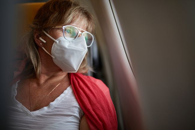 Voyageur d'âge moyen portant un masque KN95 regardant par la fenêtre de l'avion