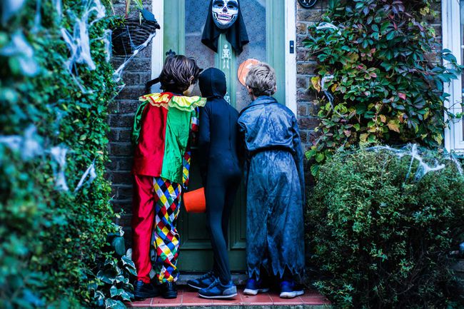 Trois garçons en costumes d'halloween, debout à la porte, tour ou traitement, vue arrière