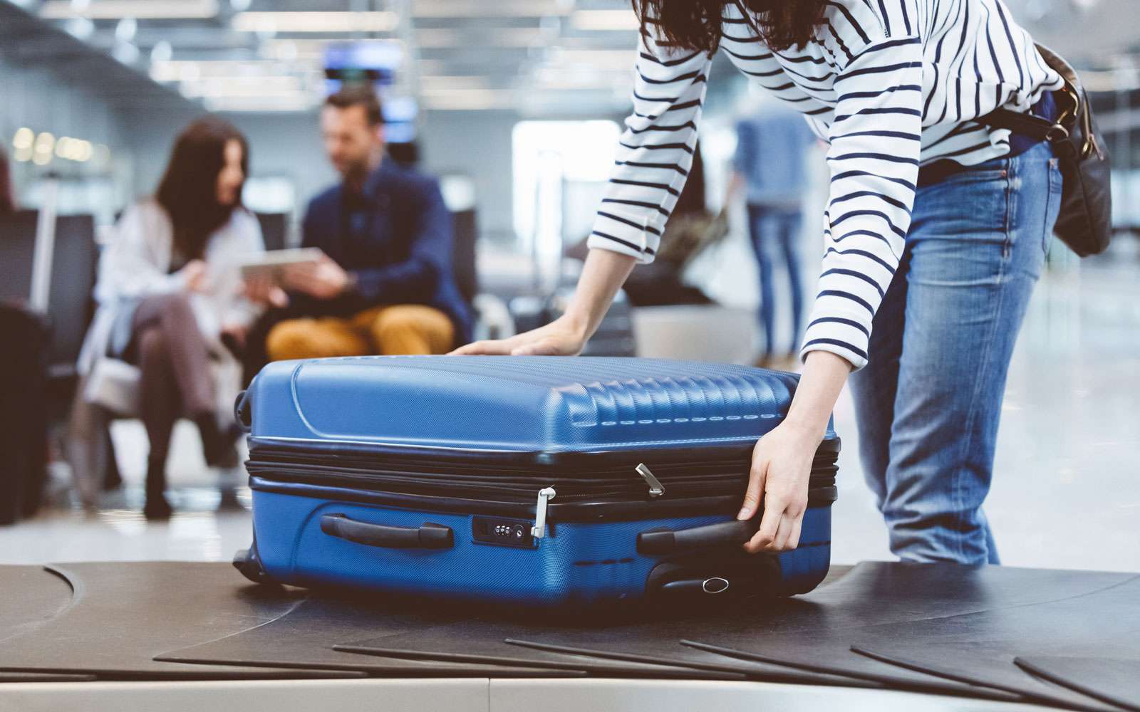 Femme tenant une valise bleue sur le carrousel à bagages