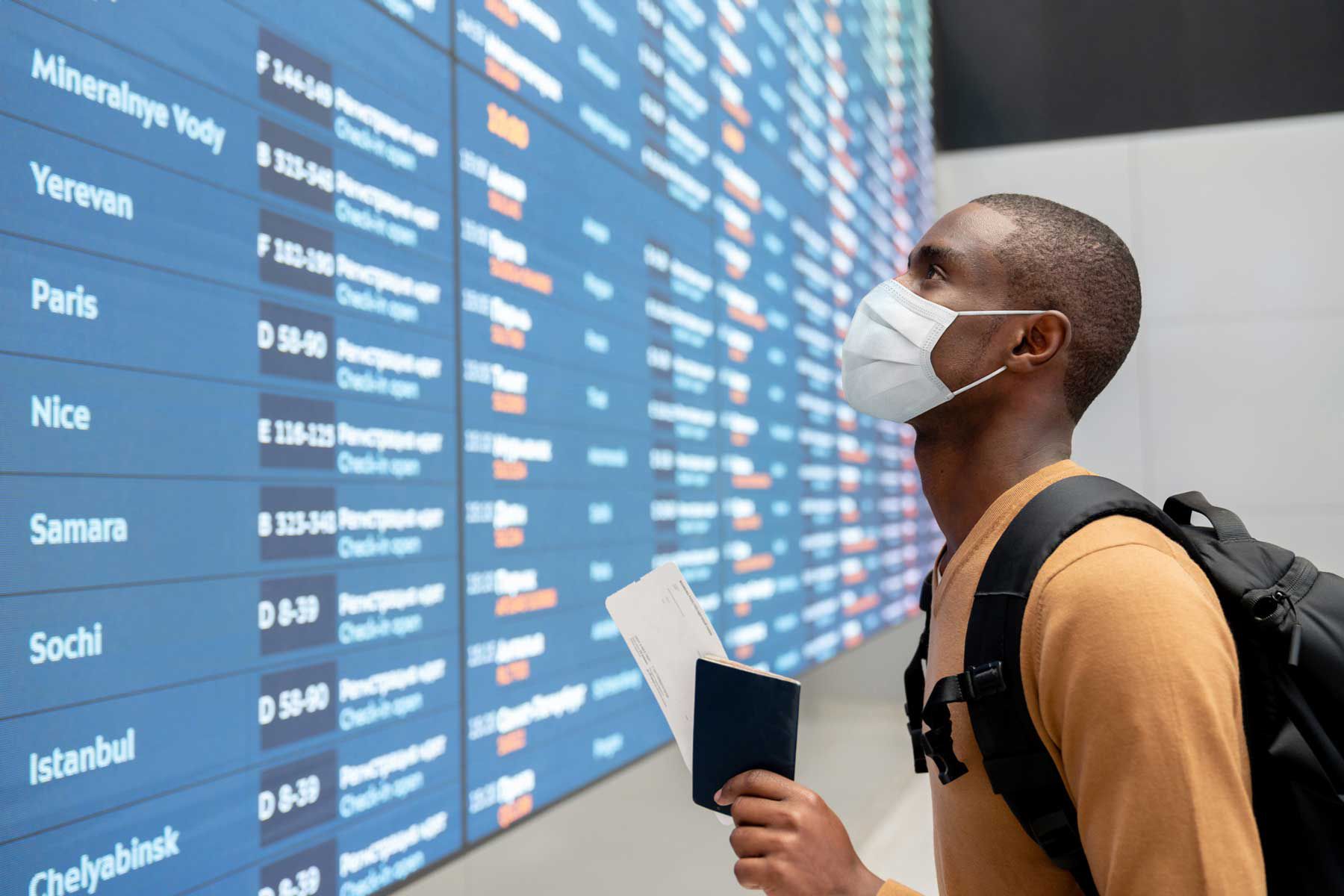 Portrait d'un voyageur noir portant un masque facial à l'aéroport et regardant l'horaire des vols