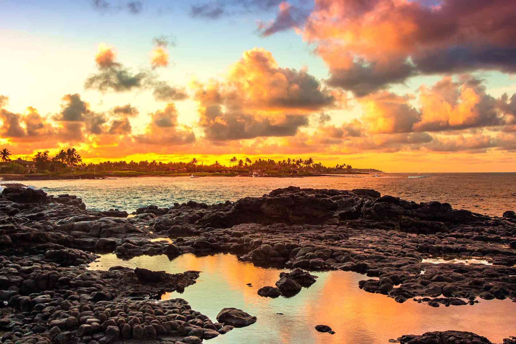 Coucher de soleil sur la baie de Kukuiula, Kauai, Hawaii avec des nuages ​​se reflétant dans le bassin d'eau dans les roches de lave