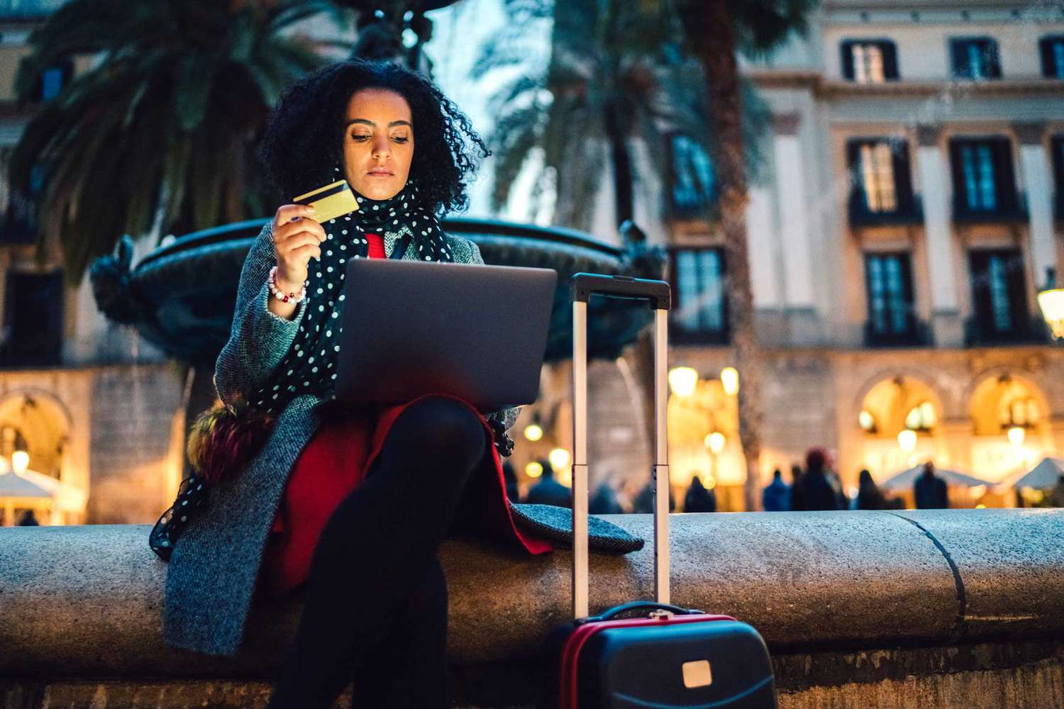Touriste assis à la fontaine de la Placa Reial et utilisant une carte de crédit pour effectuer une réservation en ligne pour un hôtel de dernière minute
