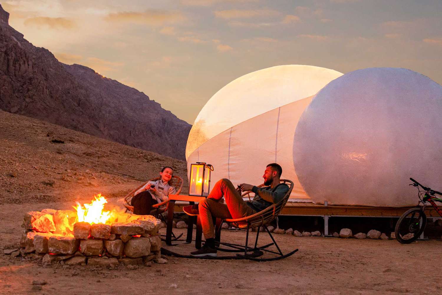 Deux personnes près d'un feu de camp à l'extérieur de tentes en forme de dôme dans le parc du désert de Jebel Hafit
