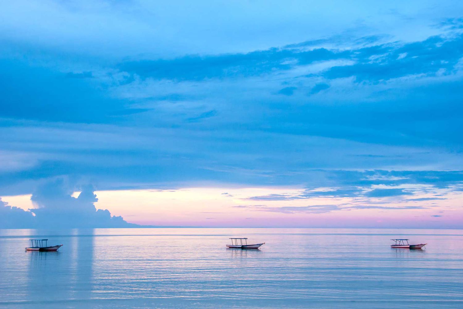 Eau bleue océanique sans fin avec trois bateaux de pêche au coucher du soleil, très apaisant