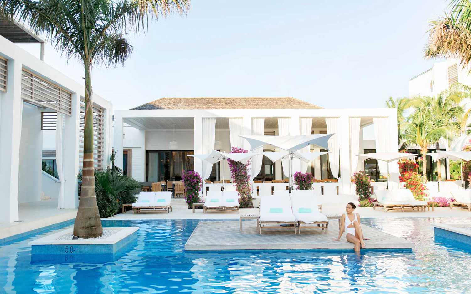 Une femme est assise à côté de la piscine centrale du Wymara Resort dans les îles Turques et Caïques