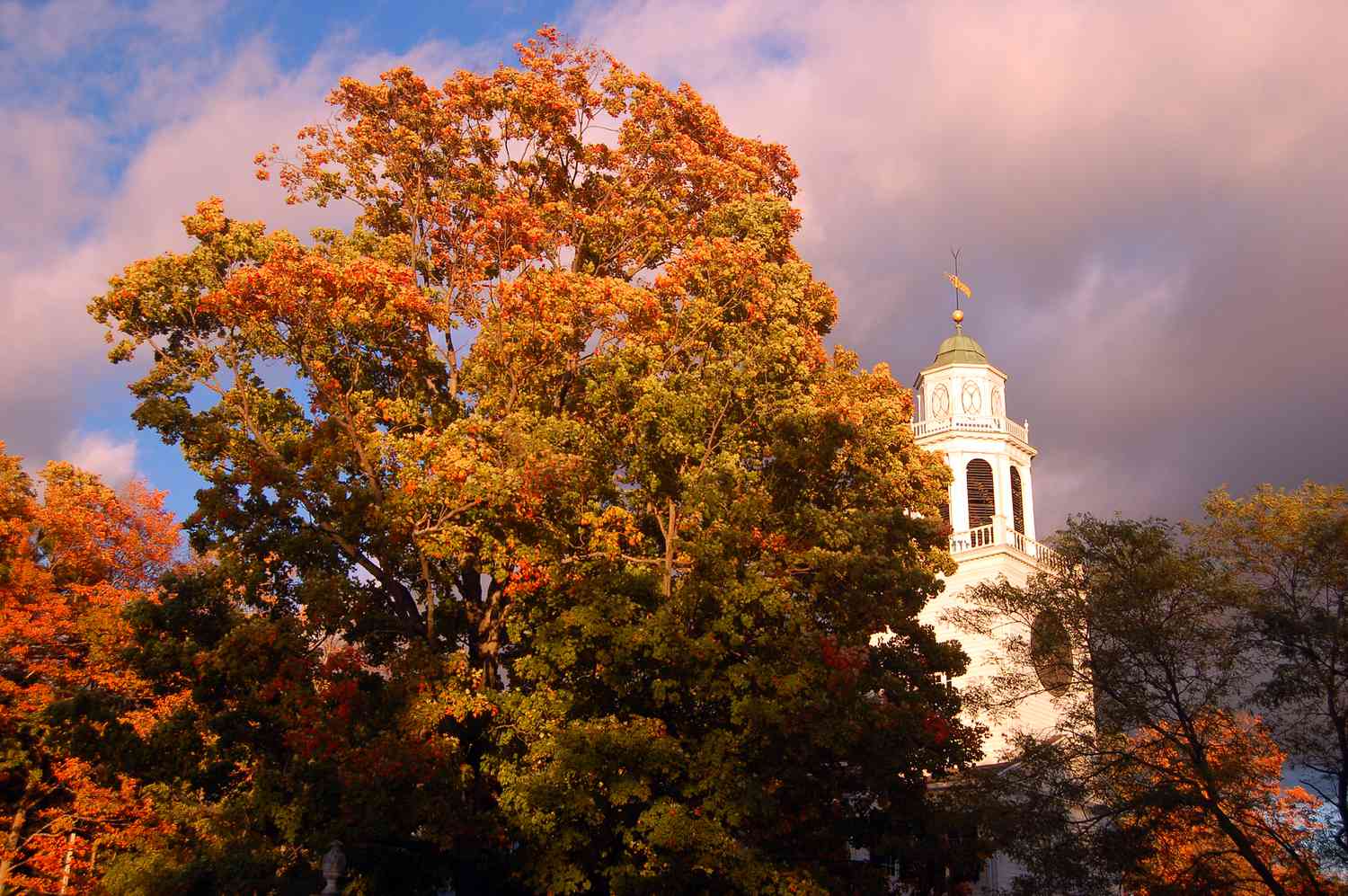 Soleil culminant à travers les nuages ​​au-dessus de l'arbre et de l'église d'automne