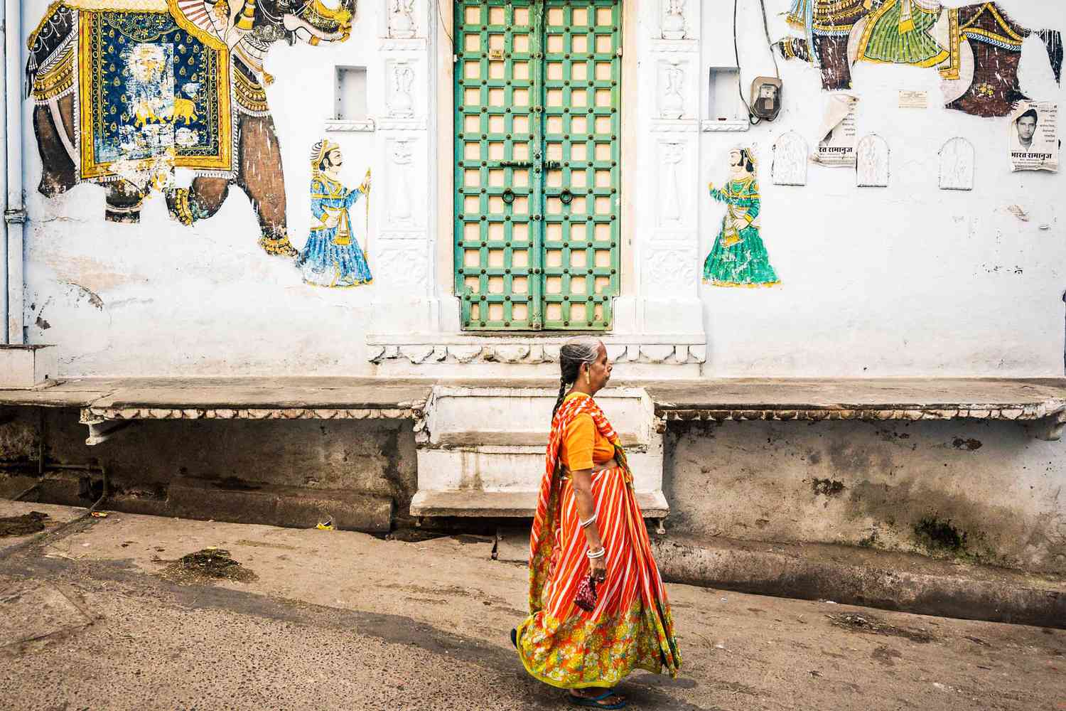 Une femme dans un sari orange passe devant une peinture murale à Udaipur, Inde